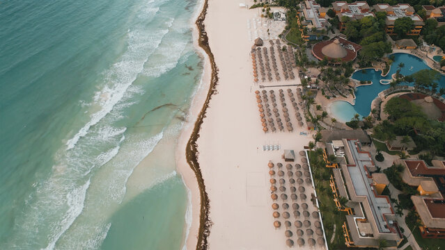 Aerial view of Playa del Carmen beach featuring rows of sun umbrellas, resort architecture, swimming pools, and turquoise Caribbean sea water in Playa del Carmen, Quintana Roo, Mexico.