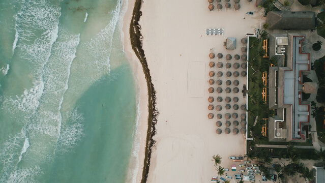 Aerial view of the sandy beach with rows of umbrellas, turquoise ocean waves, and a resort building in Playa del Carmen, Quintana Roo, Mexico.