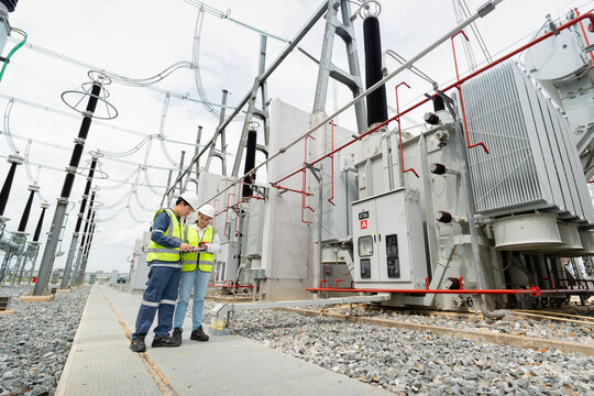 Transformer inspection at an outdoor substation shows two engineers reviewing a tablet together beside a large power transformer.