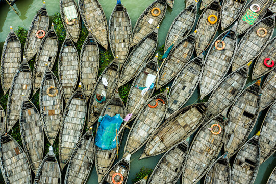 Aerial view of numerous wooden boats moored in the water, featuring textured decks, colorful lifebuoys, and blue tarps in Dhaka, Dhaka Division, Bangladesh.