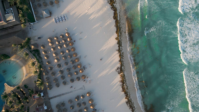 Aerial view of the white sand beach with rows of thatched umbrellas and turquoise Caribbean sea waves in Playa del Carmen, Quintana Roo, Mexico.