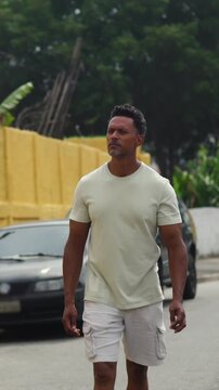 African American man walking along urban street with thoughtful expression near yellow walls