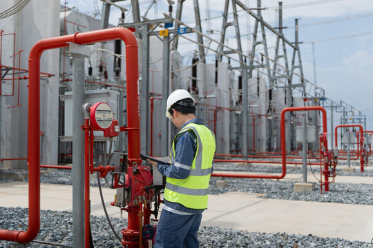 At a fire protection system in an outdoor electrical substation, a technician inspects the valve with a tablet near the gantry.