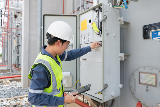 Control cabinet inspection at the substation involves an engineer in a hard hat holding a tablet to examine a switch.
