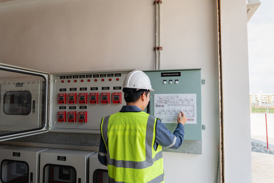 Inside a fire protection system control room, a technician inspects a schematic on the wall-mounted fire alarm control panel.