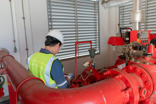 Technician inspects fire protection system and writes on a clipboard in an indoor pump room beside a red fire pump.