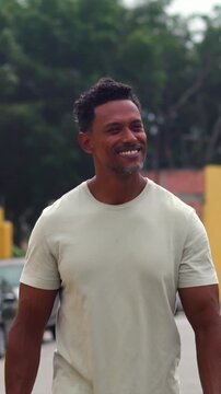 African American man walking along urban street smiling warmly with yellow walls in background