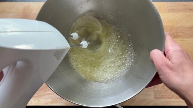 Whipping egg whites with a handheld electric mixer in a stainless steel bowl. Baking, cooking, or making meringue.