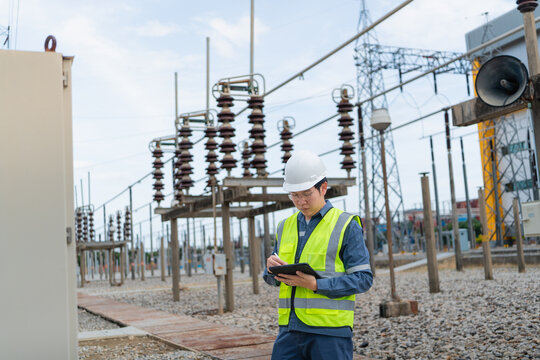 Disconnect switch inspection occurs during a substation patrol while one technician writes on a tablet beside an insulator and transmission tower.