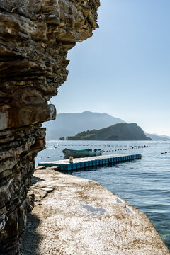 Small fishing boat at a floating plastic dock near layered rock cliff in Budva, Montenegro