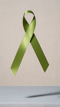 Green satin ribbon floating in a weightless loop over a soft linen surface, creating a calm atmosphere with copy space for mental health awareness