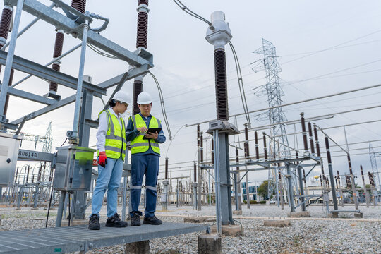 Substation patrol inspection shows two technicians consulting a tablet beside a disconnect switch on a raised platform in the switchyard.