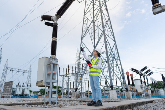 Pylon inspection beneath a lattice transmission tower shows an engineer holding a tablet and pointing at overhead equipment in the switchyard.