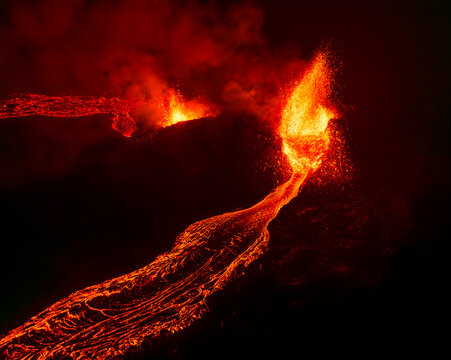 Aerial view of a volcanic eruption with glowing lava flowing from a crater at night with sparks and smoke in Iceland.