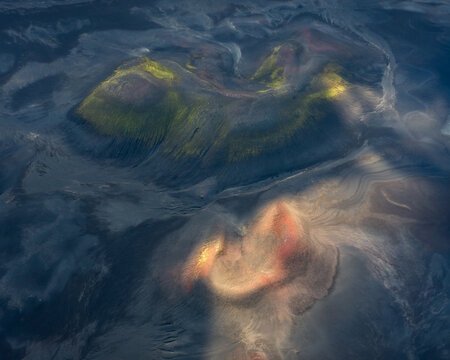 Aerial view of volcanic craters in the Iceland Highlands featuring mossy green slopes and vibrant reddish-orange volcanic soil under dramatic light in Iceland.
