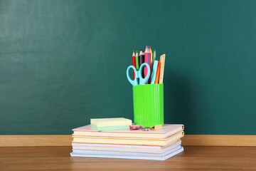 Books, notebooks and stationery on wooden table against chalkboard. Space for text © New Africa