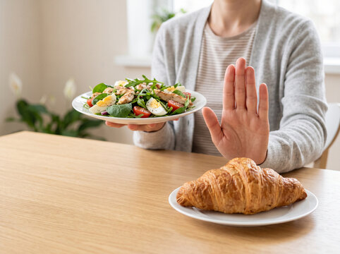 Close up of a woman hand gesturing stop to refuse eating croissant for her weight loss diet program in a bright clean dining room