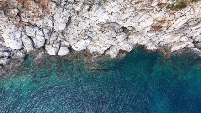 Aerial view of rocky coastline with clear blue water and vibrant vegetation along the shore, showcasing the natural beauty of a coastal landscape in a serene environment. Sea waves crashing of rocky c