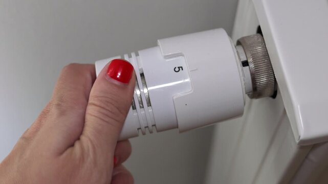Close-up video showing a person adjusting a white thermostatic radiator valve by turning the temperature control dial
