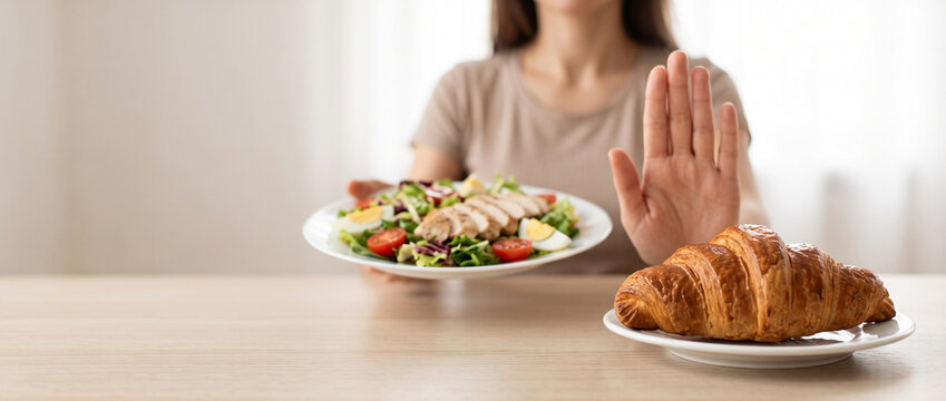 Woman refusing a croissant while choosing a plate of fresh salad and healthy food, representing mindful eating, diet change, weight management and healthier food choices