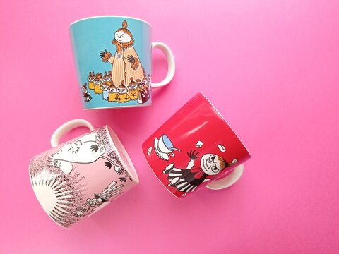 Top view of three different Moomin mugs on the pink background. 