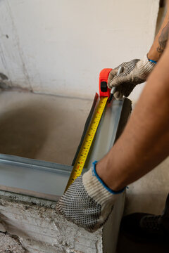 Hands wearing gloves measuring a drywall stud with a tape measure on site