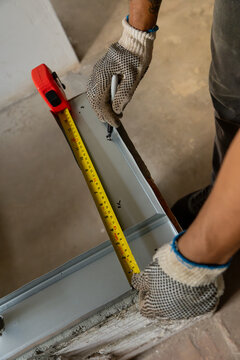 Hands wearing safety gloves measuring a drywall stud with a tape measure on site