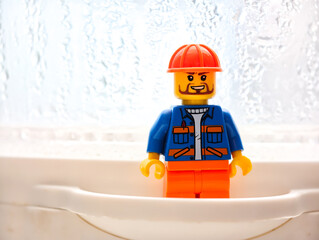 Fototapeta premium Russia, St. Petersburg, August 8, 2020 A miniature Lego man sitting in a bathroom sink, a creative and humorous scene