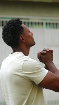 African American man smiling gently with clasped hands, looking skyward in hope and gratitude