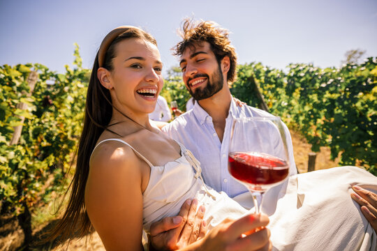 Smiling couple holding wine glasses while relaxing in a vineyard