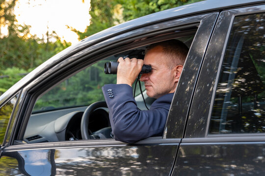 Private detective observes through binoculars from a vehicle during surveillance, investigation and evidence gathering.