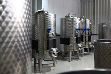 Obraz premium Containers for wine wort. Fermentation tank. Industrial winery interior with stainless steel tanks. Blue valves and round manholes. Concept of small modern winery