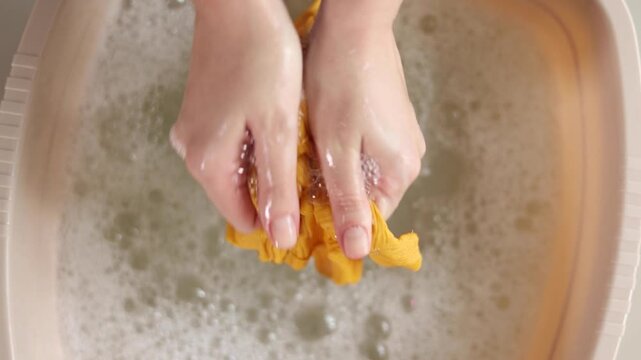 Hand washing children's clothes in soapy water with laundry detergent, gentle household care and hygiene