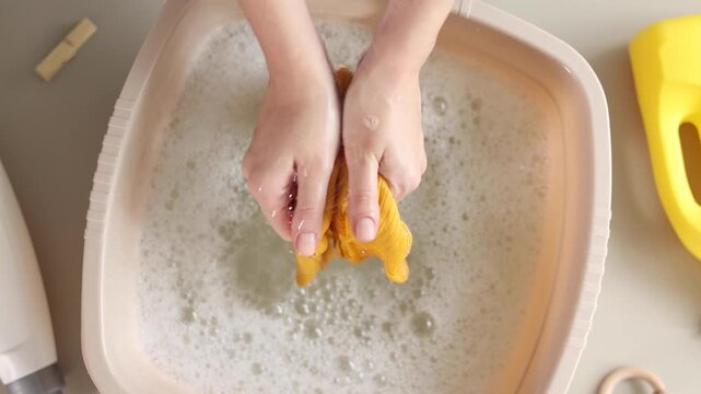Hand washing children's clothes in soapy water with laundry detergent, gentle household care and hygiene