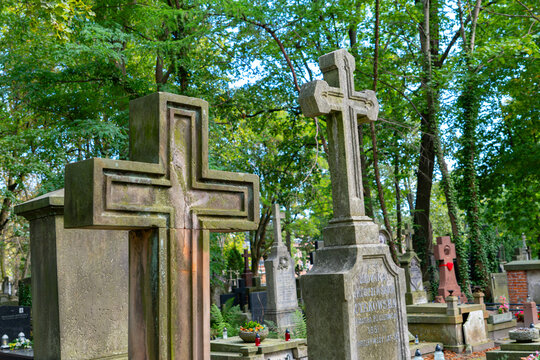 Two weathered stone crosses in a historic cemetery, large carved Christian grave monuments surrounded by lush green trees and old tombstones