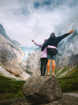 Couple friends travel together sightseeing Briksdalsbreen glacier view natural landmark in Norway, man and woman hugging in love on romantic holidays outdoor in mountains family bonding moments