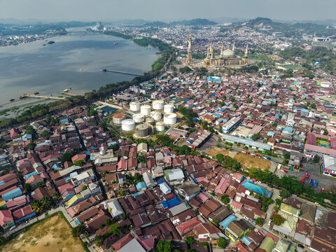 Aerial view of the PT. Pertamina TBBM Samarinda fuel storage facility near the Mahakam River, surrounded by dense urban housing in Samarinda, East Kalimantan, Indonesia.