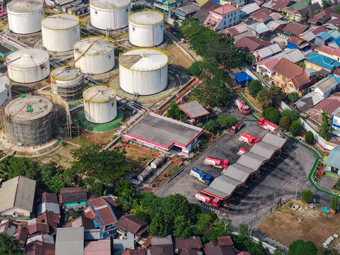 Aerial view of PT. Pertamina TBBM Samarinda fuel storage facility with white tanks, tanker trucks at the loading terminal, and nearby houses in Samarinda, East Kalimantan, Indonesia.