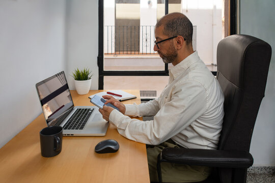 Young man checking smartphone at office desk beside laptop