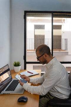 Young man checking smartphone beside laptop at desk
