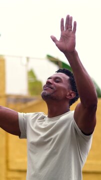 African American man standing with arms raised and face lifted upward against textured yellow wall