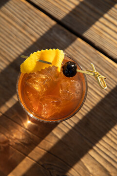 old fashioned cocktail garnished with black olive and orange peel on wood table in golden light and shadows