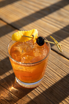 old fashioned cocktail garnished with black olive and orange peel on wood table in golden light and shadows