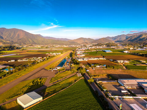 Aerial view of the agricultural landscape of Constanza with lush green plantations, surrounding mountains, and rural roads at sunrise in Constanza, La Vega Province, Dominican Republic.