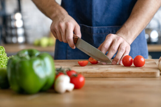 Cropped shot of man cooking in modern kitchen with fresh vegetables on table, preparing healthy homemade meal, culinary lifestyle concept, food preparation process and everyday home activity