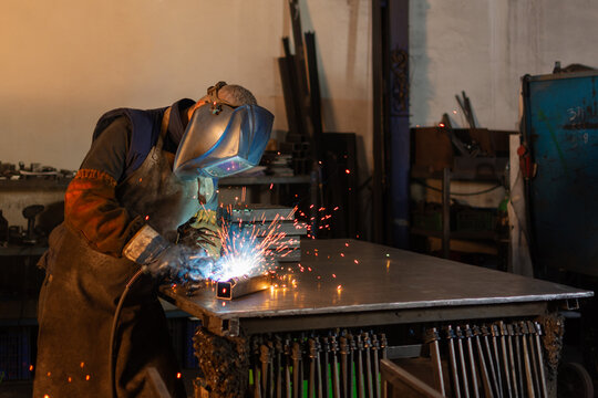 Industrial welder welding metal pieces at workshop workbench