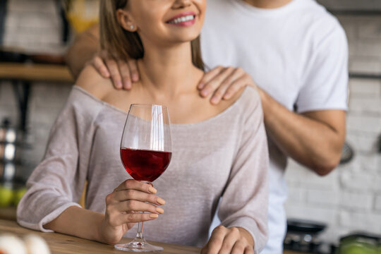 Cropped shot of beautiful girl drinking wine while handsome man giving her a massage in home kitchen, romantic couple, intimate relationship, cozy lifestyle, relaxation, love and happy moments concept