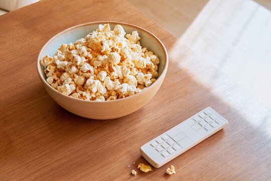 Bowl of buttery popcorn and a remote control on a warm wooden table, a cozy movie night scene with copy space for home entertainment marketing