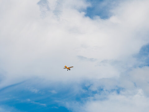 Aerial view of a small yellow light aircraft flying through a blue sky with scattered white clouds over Kyjov, South Moravian Region, Czechia.