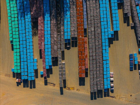 Aerial view of stacked industrial materials wrapped in blue, green, and brown plastic sheeting arranged in neat rows within a storage yard in Kyjov, South Moravian Region, Czechia.